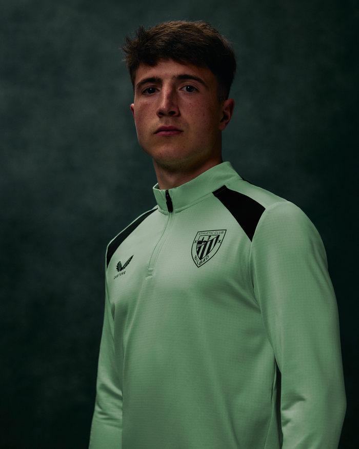 Model wearing mint green performance midlayer top with zip collar dark shoulder panels and crest logo