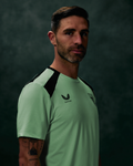 Male model wearing neon mint green athletic tee with navy shoulder panels and crest on chest