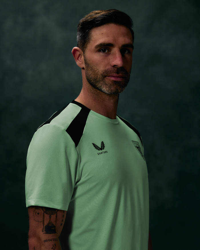 Male model wearing neon mint green athletic tee with navy shoulder panels and crest on chest